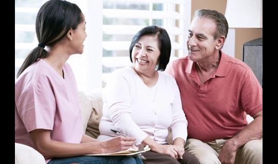 A visiting nurse talks to a man and a woman in their home.