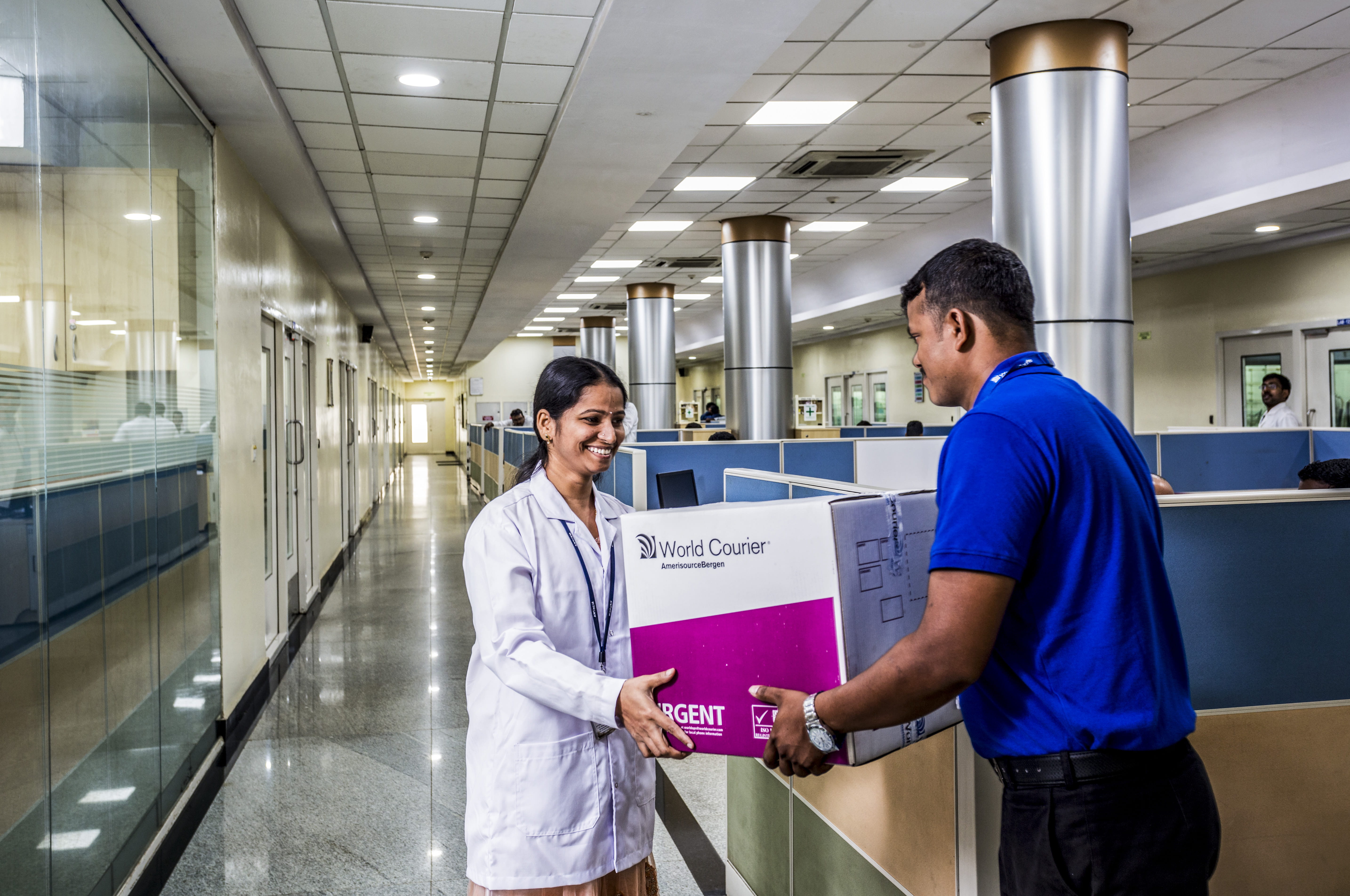 A World Courier associate delivers a shipment to a woman in a lab coat inside a hospital.
