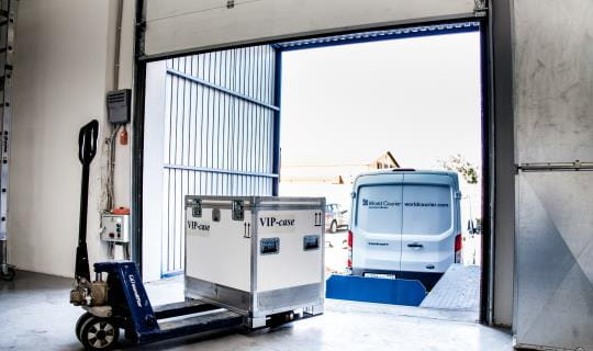 A shipping container is prepared to be loaded into a van at a loading dock.